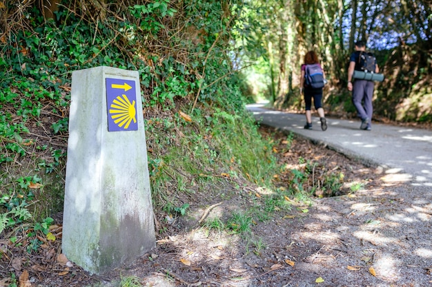 Foto hito del camino de santiago con peregrinos irreconocibles caminando en el fondo