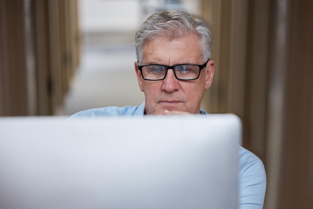 Hmm, was ist der beste Weg, um diese Aufnahme eines reifen Geschäftsmanns zu machen, der allein im Büro sitzt und seinen Computer benutzt