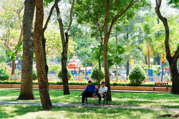 Ho chi minh, vietnã - 26 de fevereiro de 2016: pessoas sentadas no banco no parque verde na cidade de ho chi minh, no vietnã, na ásia. antiga cidade vietnamita chamada saigon. exterior e paisagem urbana