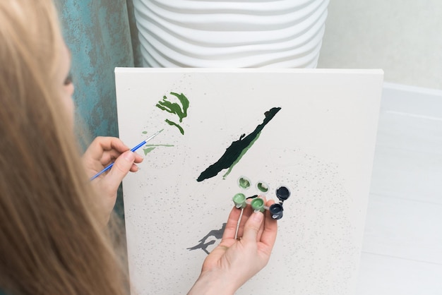 Foto hobbies em casa: auto-isolamento, pintura por números para desenhar da vista de cima de uma mulher segurando um pincel com tintas, pintura. o interior da casa é leve.