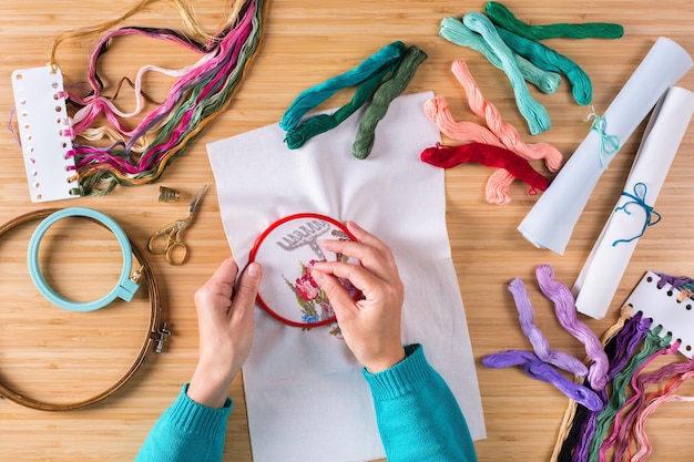 Hobby, artesanía, creatividad, concepto de tiempo libre en casa. Manos femeninas bordando punto de cruz en el lienzo. Endecha plana, vista superior