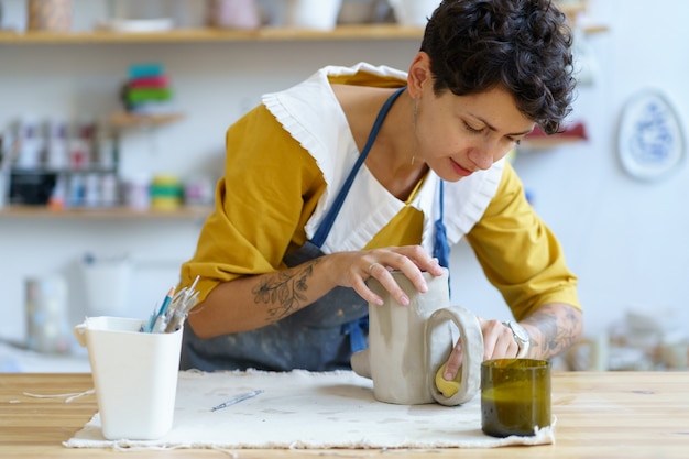 Foto hobby de cerâmica ou manufatura de cerâmica pequena empresa jovem artista moldando jarra de argila crua em estúdio