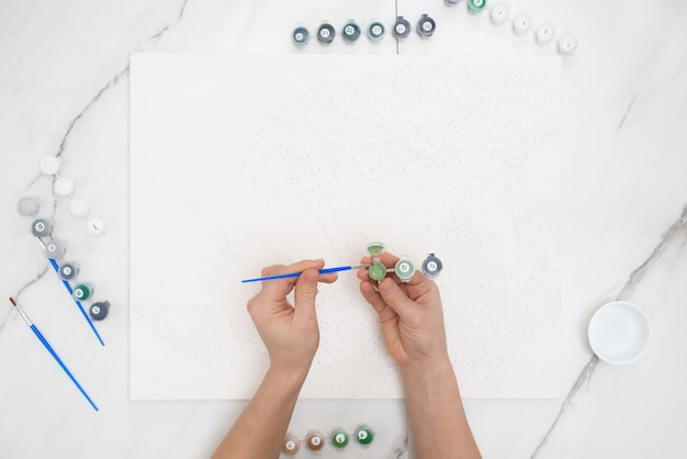 Hobby em casa pintar por números para desenhar de cima, uma visão das mãos de mulheres segurando latas de tintas