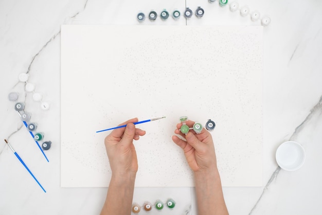 Foto hobby em casa pintar por números para desenhar de cima, uma visão das mãos de mulheres segurando latas de tintas