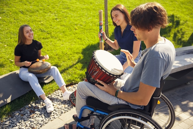 Foto hobby. glücklicher behinderter mann im rollstuhl, der zeit mit freunden verbringt, die live-instrumentalmusik im freien spielen. konzept des sozialen lebens, freundschaft, möglichkeiten, inklusion, vielfalt.