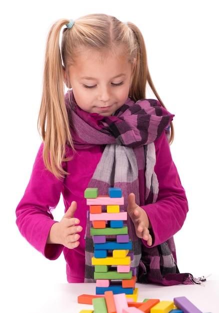 Hobbys der Kinder Kreativität ein kleines Mädchen in einem blauen Kleid, das mit dem Holzspiel Jenga auf weißem Hintergrund spielt