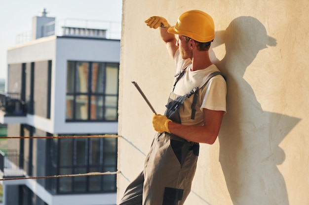 Hoch oben stehend Junger Mann, der tagsüber in Uniform auf dem Bau arbeitet