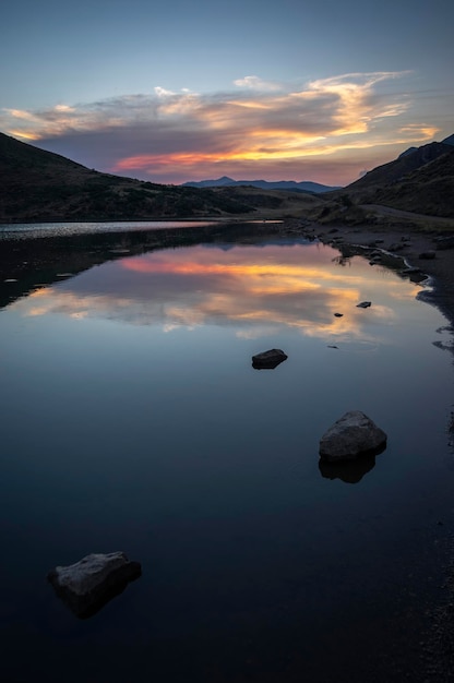 Hochformatiges Foto eines Sonnenuntergangs an einem Bergsee mit Wolkenreflexionen auf dem glasklaren Wasser