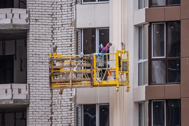 Hochhausfassadenarbeiten. Der Baumeister in der gelben Wiege. Arbeit in der Höhe. Immobilienmarkt.