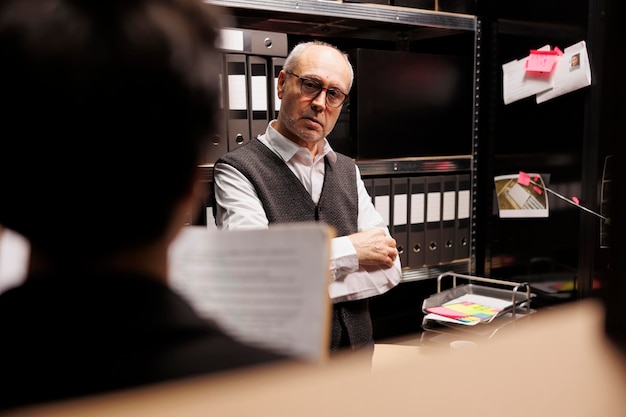 Foto hochrangiger polizeibeamter erklärt einem privatdetektiv vertrauliche informationen und arbeitet überstunden an einem strafverfahren im archivraum. ermittler diskutieren über mysteriöse vermisstenanzeige