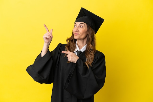 Hochschulabsolvent mittleren Alters isoliert auf gelbem Hintergrund, der mit dem Zeigefinger zeigt, eine großartige Idee
