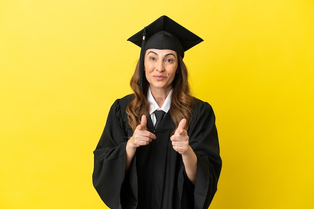 Hochschulabsolvent mittleren Alters isoliert auf gelbem Hintergrund, der nach vorne zeigt und lächelt