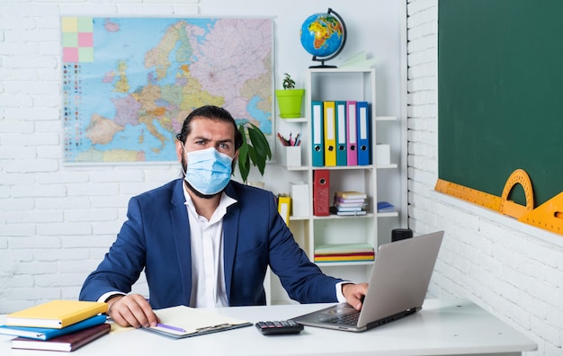 Hochschuldozent für Coronavirus-Pandemie. zurück zur Schule. Nicht formale Bildung. reife lehrer tragen eine atemschutzmaske. brutaler bärtiger mann arbeitet während covid 19 im klassenzimmer. bereiten sie sich auf die online-prüfung vor.