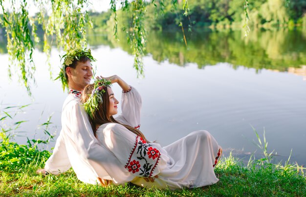 Hochsommer. Junge Liebespaar in slawischen Kostümen am Ufer des Sees. Slawischer Feiertag von Ivan Kupala.