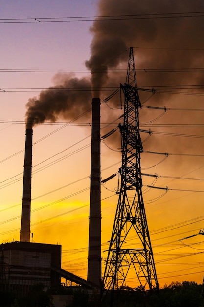 Hochspannungspfosten Hochspannungsturm Himmelshintergrund Fabrikrohr mit Rauch darüber Erdverschmutzungskonzept Industrialisierung Selektiver Fokus