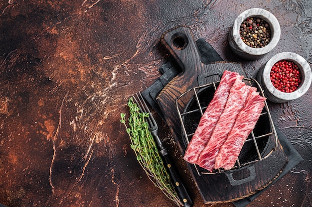 Hochwertige rohe geschnittene Wagyu-Rind-A5-Steaks auf einem Grill für Yakiniku. Japanische Lebensmittel. Dunkler Hintergrund. Ansicht von oben. Platz kopieren.