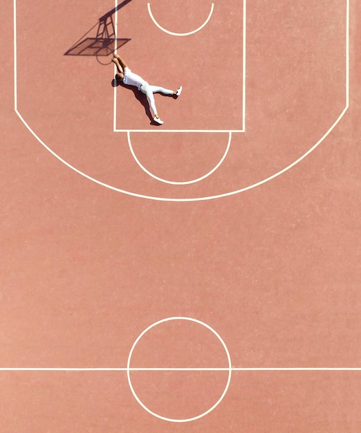 Hochwinkelansicht des auf dem Platz liegenden Mannes durch den Schatten des Basketballhoops