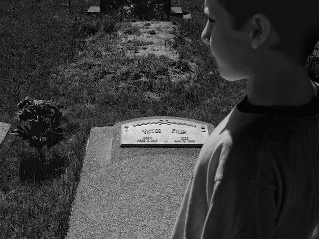 Hochwinkelansicht des Jungen am Grabstein auf dem Friedhof