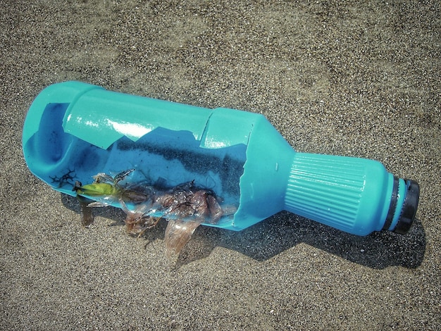 Hochwinkelansicht einer blauen gebrochenen Flasche am Sandstrand