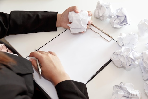 Foto hochwinkelansicht einer frau, die einen stift und einen zerknitterten papierkugel auf dem clipboard über dem tisch hält