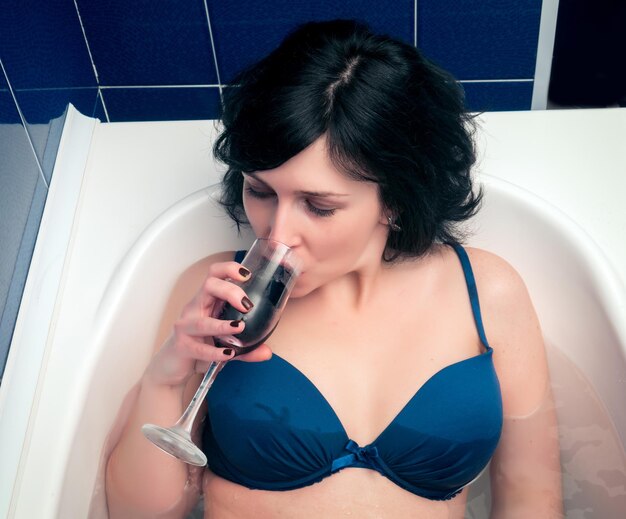 Foto hochwinkelansicht einer frau in bikini, die wein trinkt, während sie in der badewanne sitzt