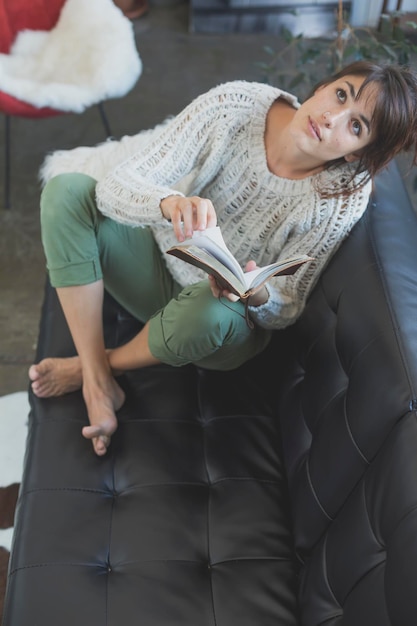 Foto hochwinkelansicht einer jungen frau mit einem buch, die auf dem sofa sitzt