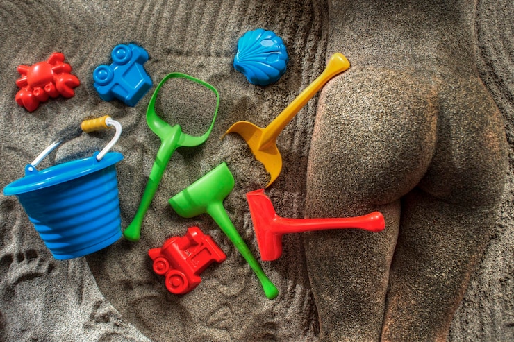 Foto hochwinkelansicht einer nackten frau, die neben einem spielzeug auf dem sand liegt