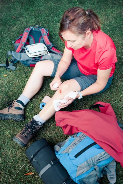 Foto hochwinkelansicht einer verletzten frau, die während des sitzens auf dem feld medizin auf das knie sprüht