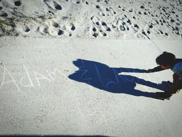 Hochwinkelansicht eines Kindes, das mit Kreide auf einem Gehweg am Strand schreibt