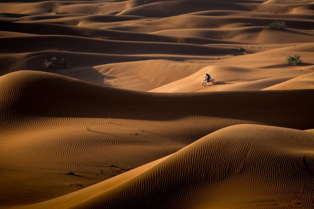 Hochwinkelansicht eines Mannes, der auf einem Motorrad auf Sand in der Wüste fährt