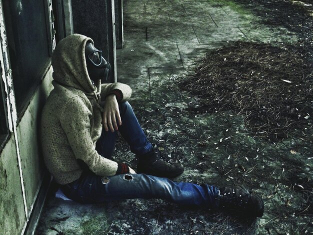 Foto hochwinkelansicht eines mannes mit gasmaske, der außerhalb eines alten gebäudes sitzt