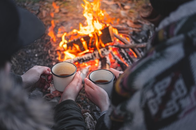 Hochwinkelansicht eines Paares, das Kaffee in Tassen gegen ein Lagerfeuer trinkt