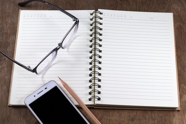 Hochwinkelansicht von Brillen mit Bleistift und Mobiltelefon mit offenem Buch auf dem Tisch