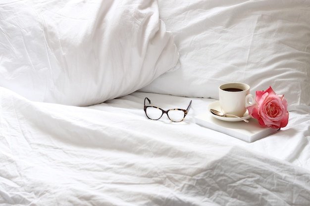 Hochwinkelansicht von Kaffeekuppe mit Rose durch Brille auf dem Bett