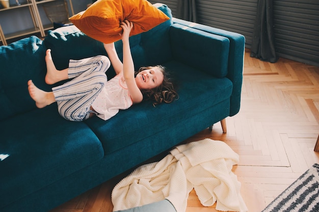 Hochwinkelansicht von Mädchen mit Kissen, das zu Hause auf dem Sofa liegt