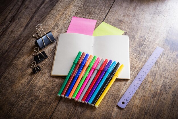 Hochwinkelansicht von mehrfarbigen Feltspitzenstift und Lineal mit Buch und Papierklemme auf dem Tisch