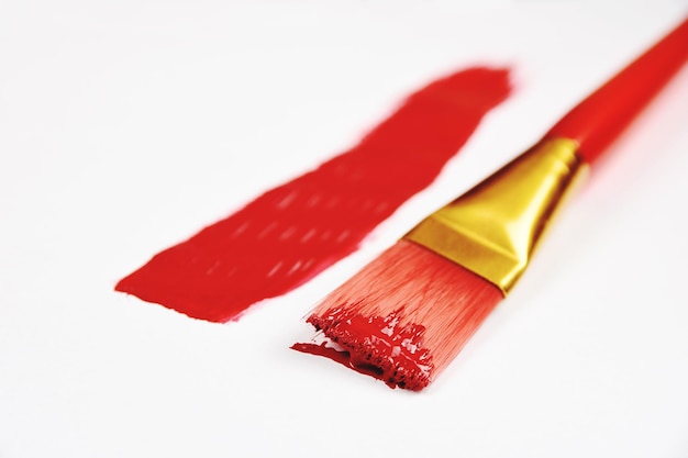 Hochwinkelansicht von Pinsel und roter Farbe auf weißem Hintergrund