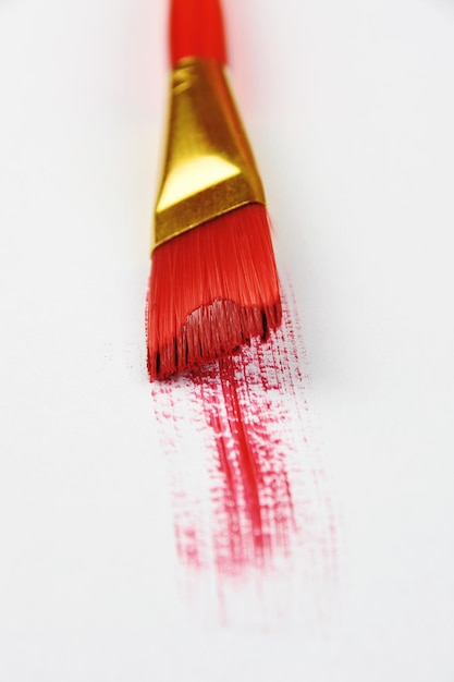 Hochwinkelansicht von Pinsel und roter Farbe auf weißem Hintergrund