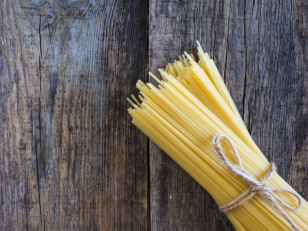 Hochwinkelansicht von rohen Spaghetti, die mit einem Seil auf einem Holztisch gebunden sind