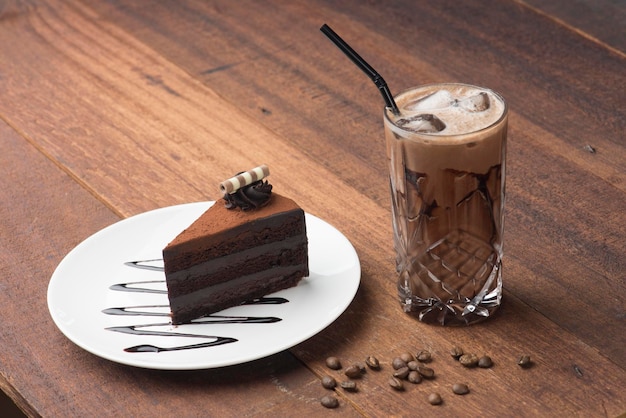 Hochwinkelansicht von Schokoladenkuchen auf dem Teller durch eiskalten Kaffee auf dem Tisch