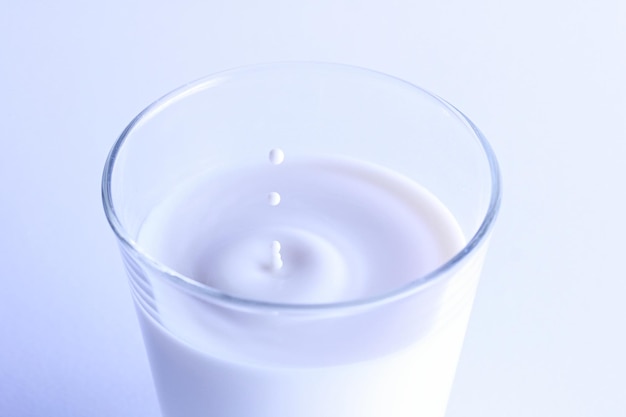 Hochwinkelansicht von spritzenden Tropfen in einem Glas Milch vor weißem Hintergrund