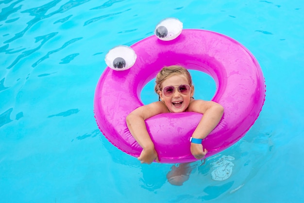 Hochwinkelaufnahme eines lächelnden Kindes im Schwimmbad mit einem rosa Ring