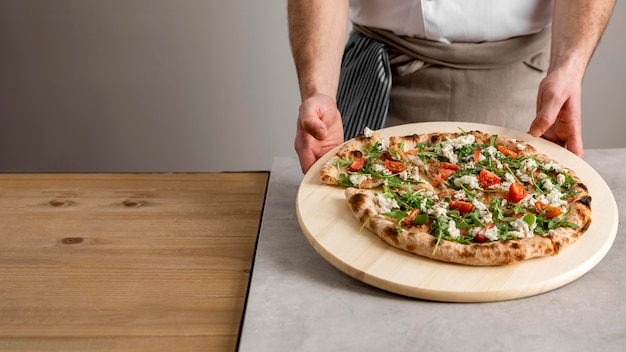 Foto hochwinkelmann, der schneidebrett mit frischer pizza hält