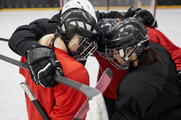 Hochwinkelporträt der weiblichen Eishockeymannschaft, die für Motivation vor Sportmatch kauert