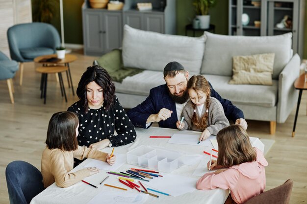 Hochwinkelporträt einer jüdischen Familie, die sich zusammenzieht, während sie zu Hause mit drei Kindern am Tisch sitzt