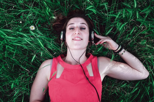 Hochwinkelporträt einer jungen Frau, die auf einem grasbewachsenen Feld liegt und Musik hört