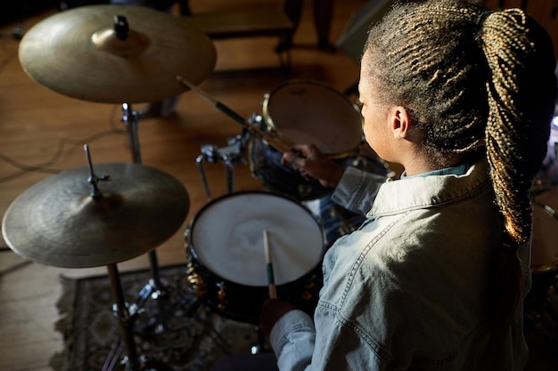 Hochwinkelporträt einer schwarzen jungen Frau, die im Dunkeln Schlagzeug spielt, mit hellem Akzentkopierraum