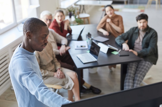 Hochwinkelporträt eines afroamerikanischen Mannes, der einem vielfältigen Geschäftsteam im Büro eine Präsentation gibt und auf den digitalen Bildschirm zeigt, Platz kopieren