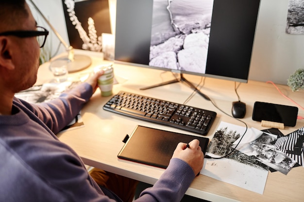 Hochwinkelporträt eines männlichen Schöpfers, der Fotos am Arbeitsplatz im Heimbüro bearbeitet und einen Stifttisch verwendet