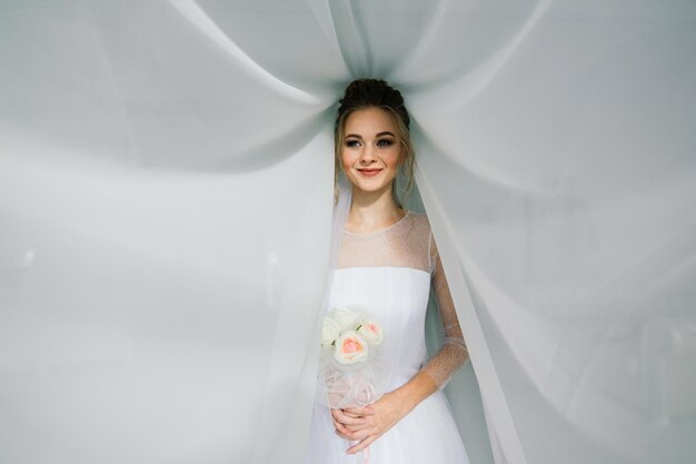 Hochzeit. Braut im schönen Kleid drinnen im weißen Studio-Interieur wie zu Hause.